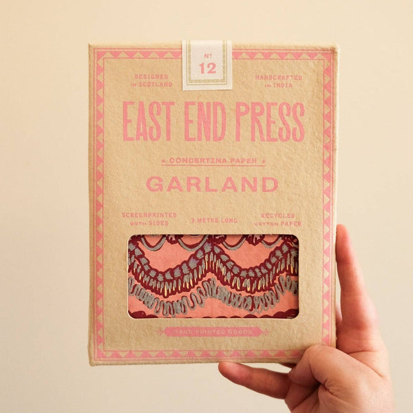 Hand holding a package labeled 'East End Press Garland' against a beige background