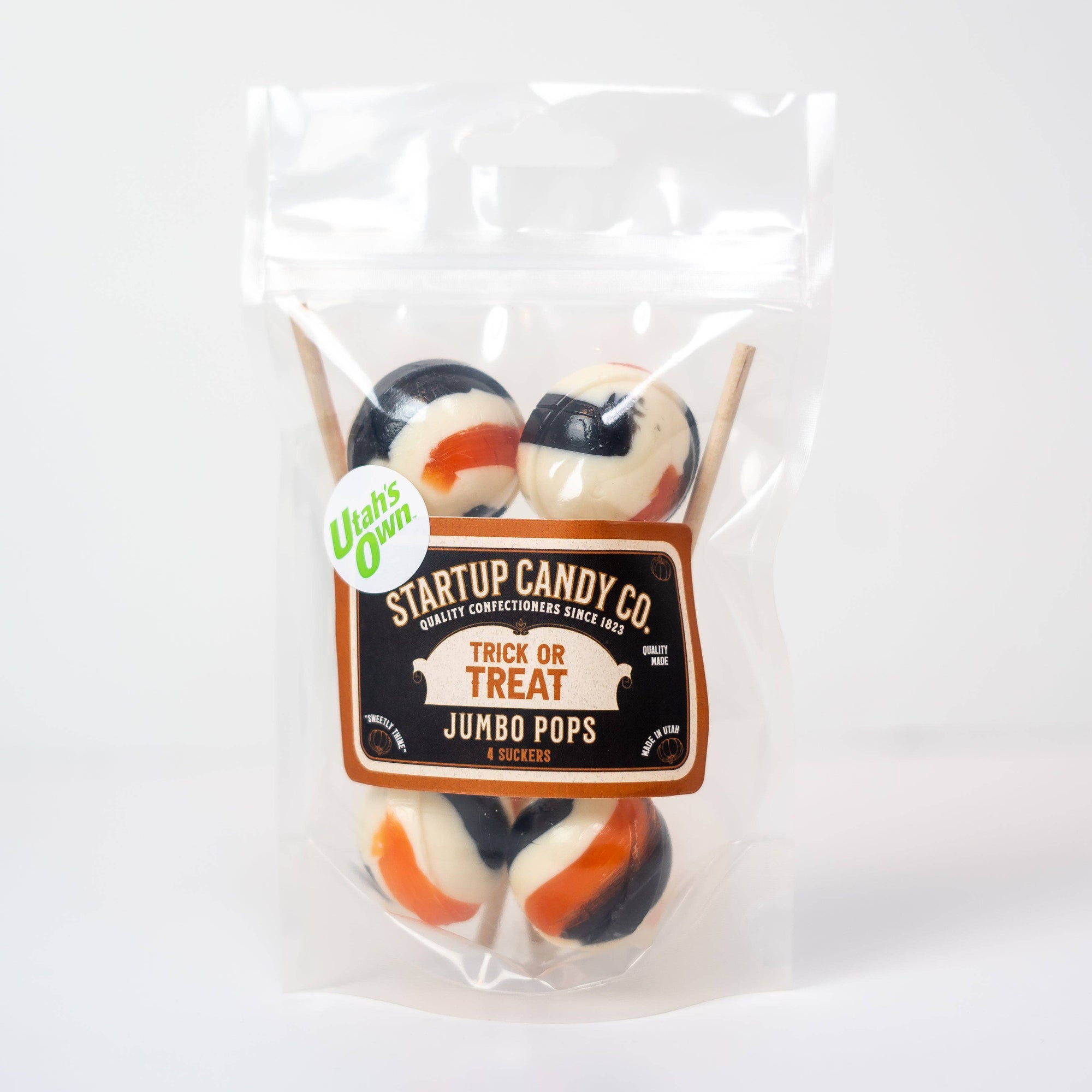 A clear plastic bag of Startup Candy Co. Jumbo Pops Halloween candy, containing four black, white, and orange striped lollipops, on a white background.