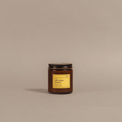 A small amber glass jar candle with a black metal lid and a yellow label reading 'honey blossom' and 'made in Italy,' centered on a plain warm beige background.