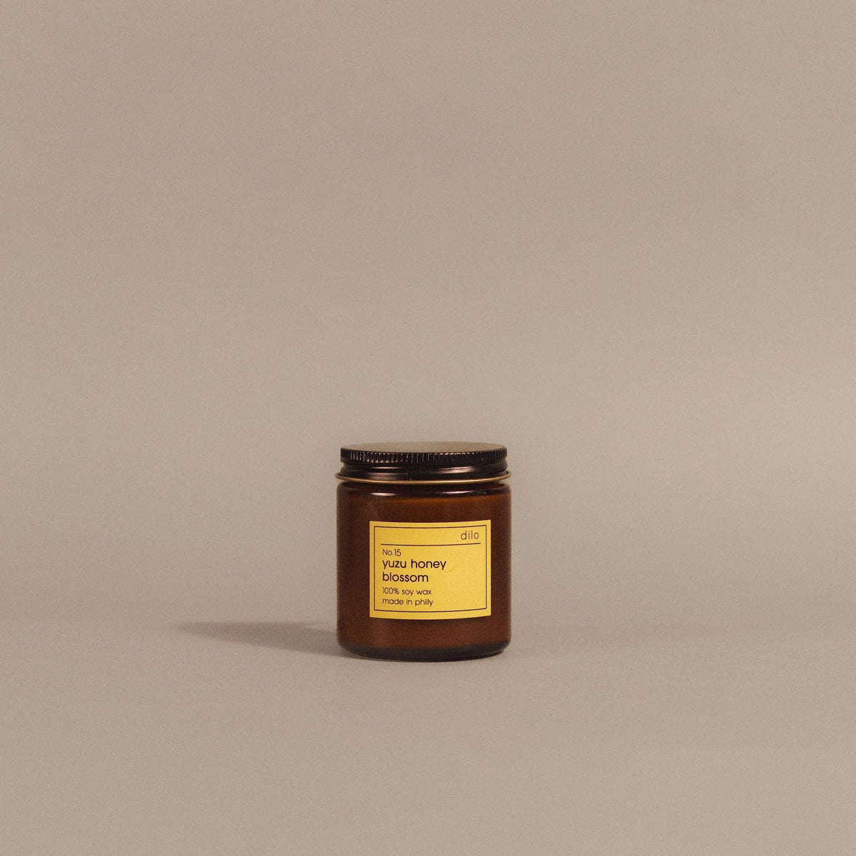 A small amber glass jar candle with a black metal lid and a yellow label reading 'honey blossom' and 'made in Italy,' centered on a plain warm beige background.