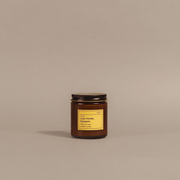 A small amber glass jar candle with a black metal lid and a yellow label reading 'honey blossom' and 'made in Italy,' centered on a plain warm beige background.