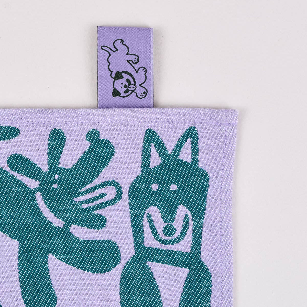 Fabric with green dog pattern on a purple background, featuring a brand tag.