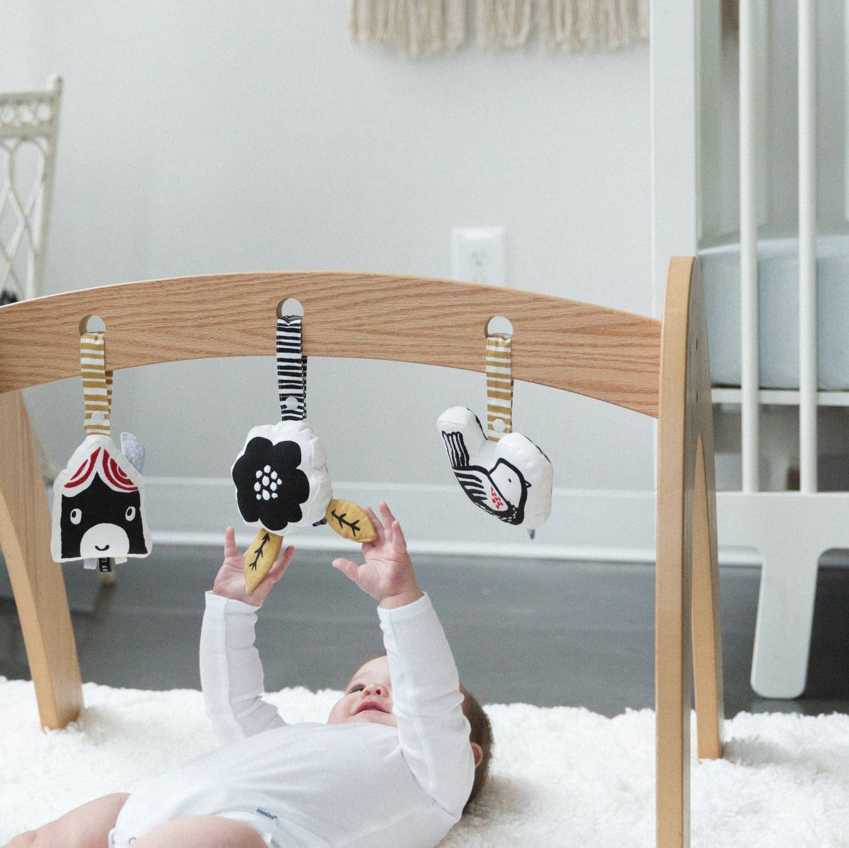 Baby playing with a wooden baby gym with hanging toys in a nursery.