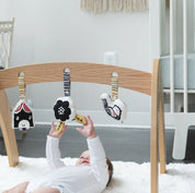 Baby playing with a wooden baby gym with hanging toys in a nursery.