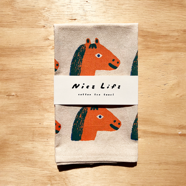 Folded towel with horse design and 'Nice Life' label on a wooden surface