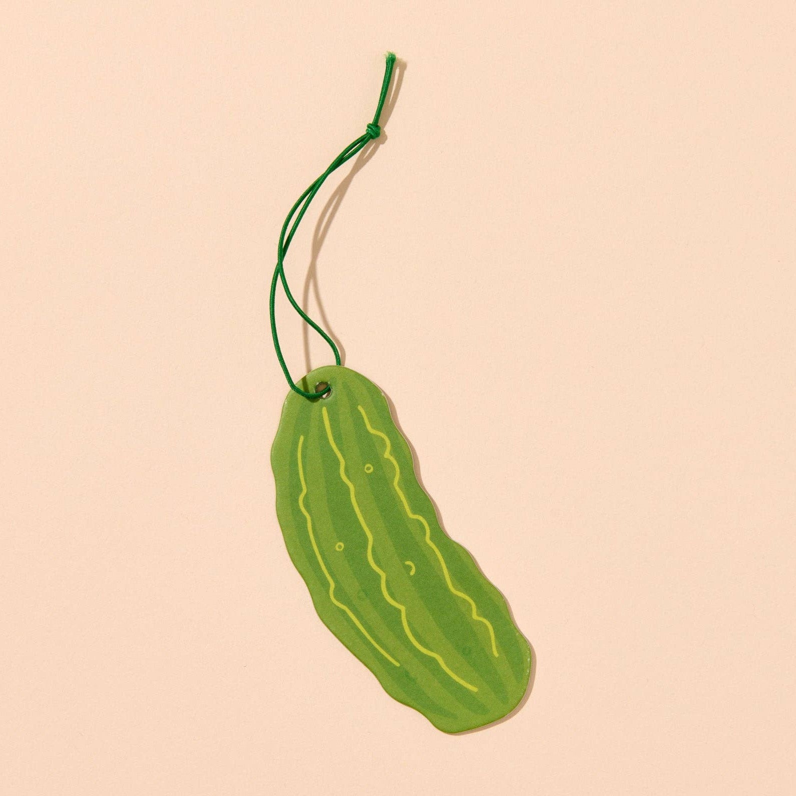 Green pickle-shaped air freshener with green string loop on a beige background