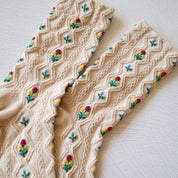 Beige knitted fabric with embroidered colorful flowers on a light background