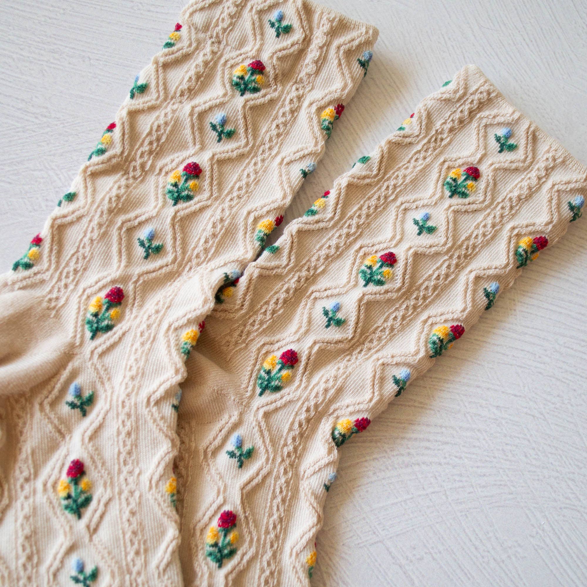 Beige knitted fabric with embroidered colorful flowers on a light background