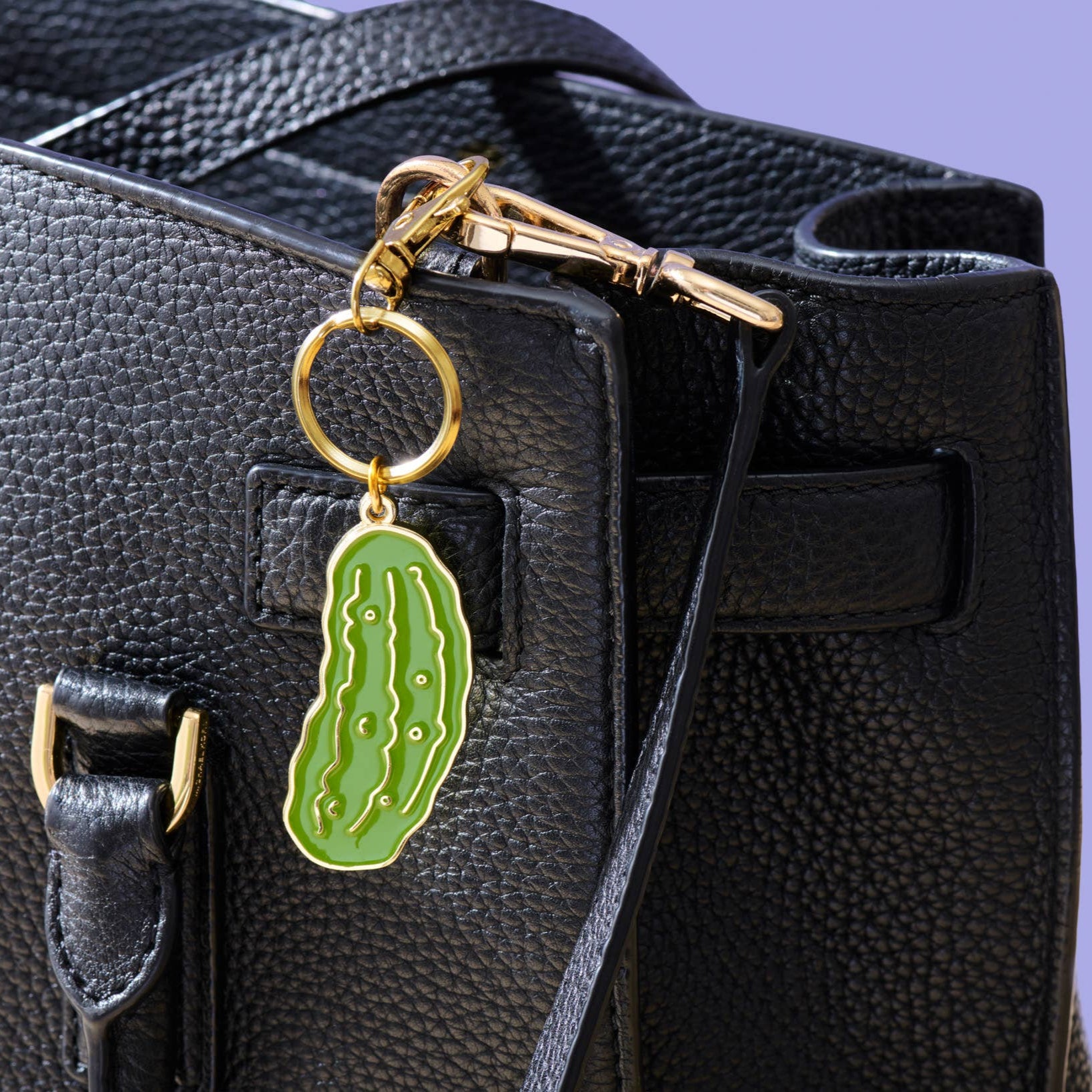 Green pickle-shaped keychain attached to a black bag on a purple background