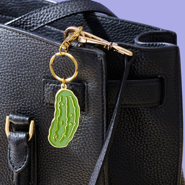 Green pickle-shaped keychain attached to a black bag on a purple background