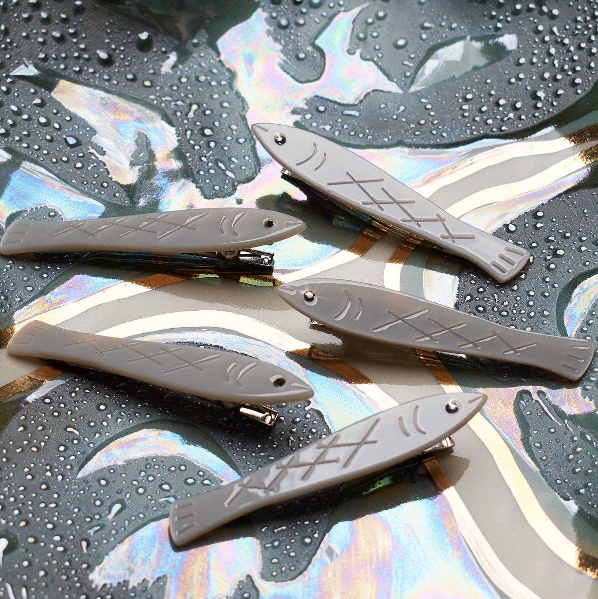Fish-shaped hair clips on a reflective surface with water droplets.
