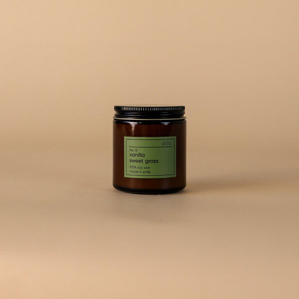 Candle in a dark glass jar with a green label on a beige background