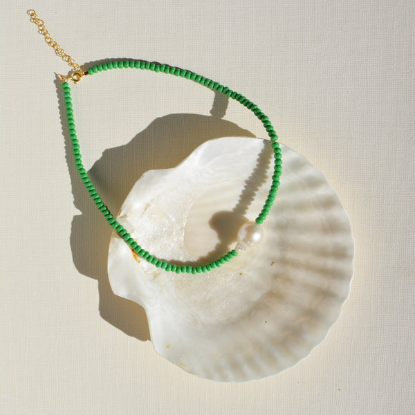 Green beaded necklace on a white shell with a beige background