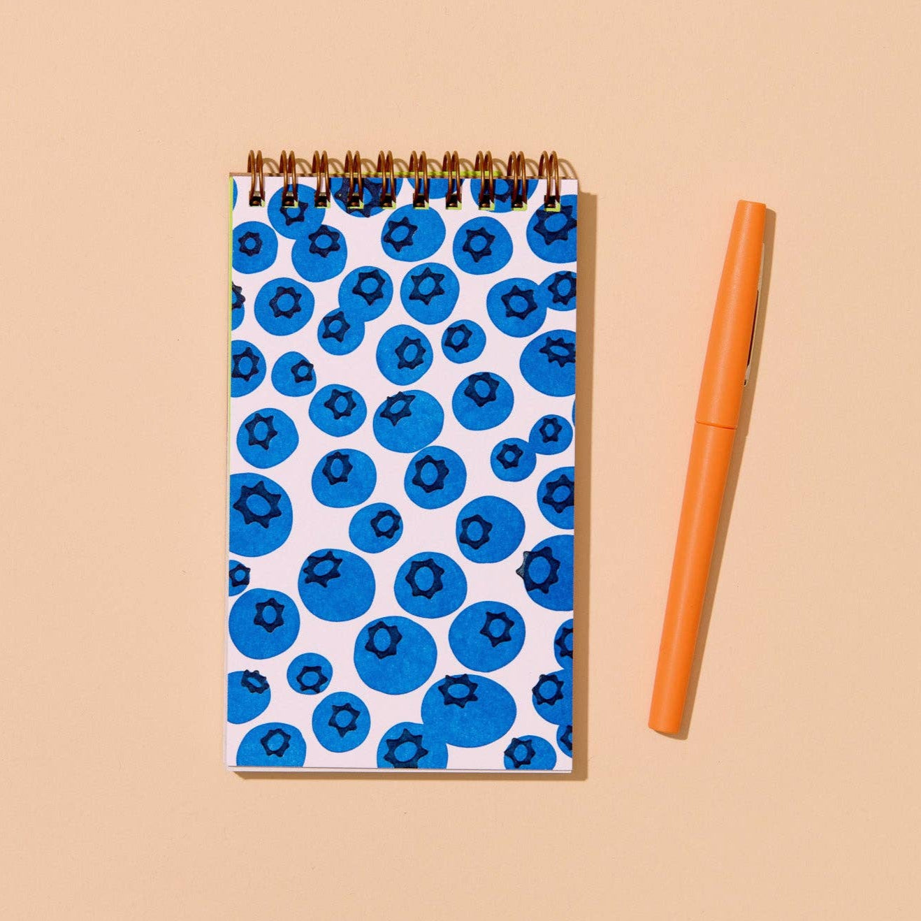 Notebook with blueberry pattern and orange pen on beige background