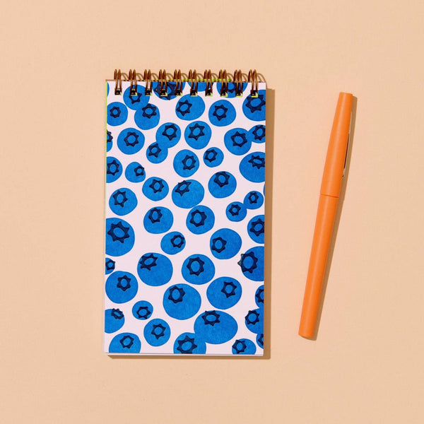 Notebook with blueberry pattern and orange pen on beige background