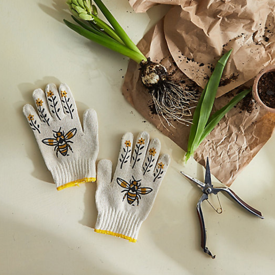 Gardening gloves with bee design on a table with plants and tools