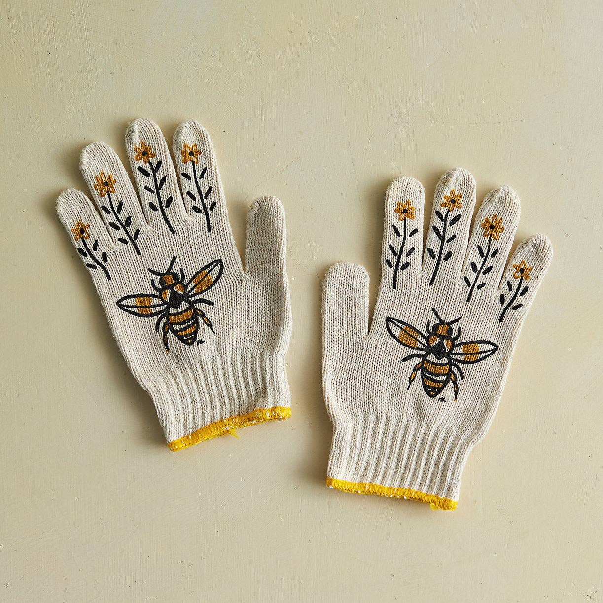 Pair of gloves with bee and flower designs on a beige background
