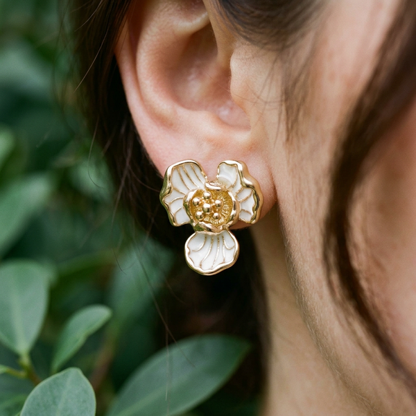 Close-up of a person wearing a gold and white floral earring with a blurred green background
