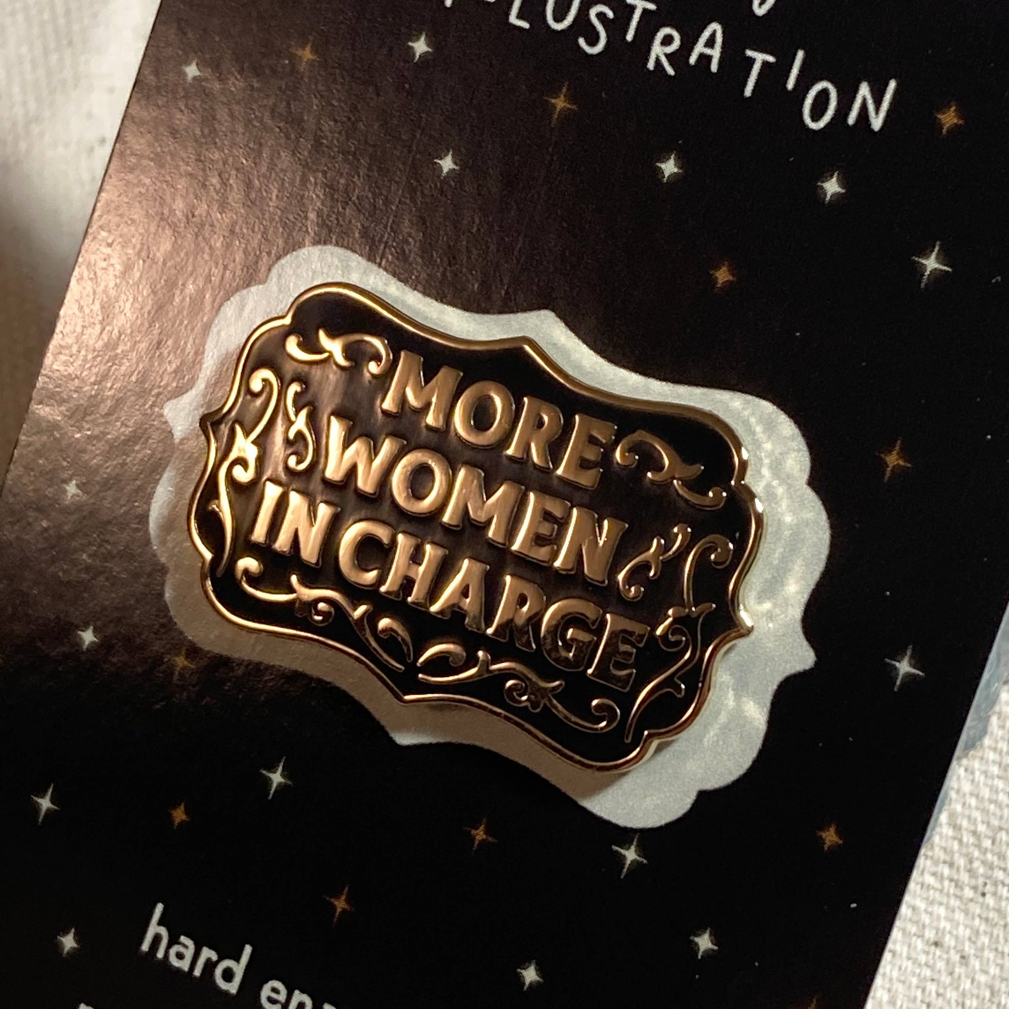 Hard enamel pin with 'More Women in Charge' text on a black card with 'molly illustration' branding.
