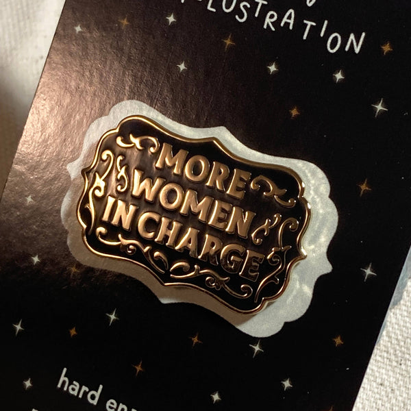 Hard enamel pin with 'More Women in Charge' text on a black card with 'molly illustration' branding.