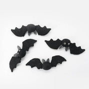 Four black felt bat decorations with small white eyes and gray wings, arranged on a plain white background.