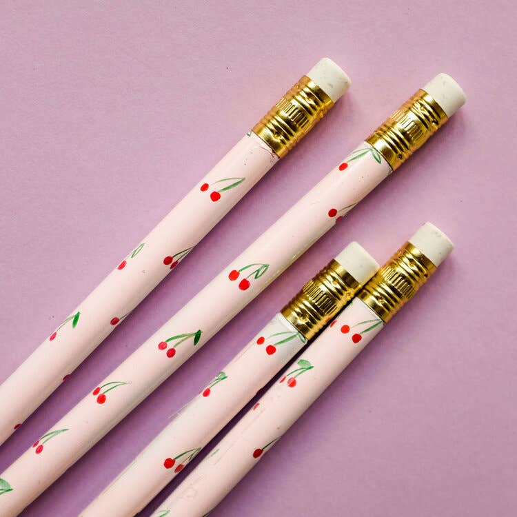 Four pink pencils with cherry designs on a purple background