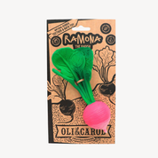 A packaged children's toy shaped like a radish, with a green leafy top and a pink root, attached to a kraft paper backing card labeled 'RaMona The Radish' and 'Oli & Carol Fruit & Veggie'.
