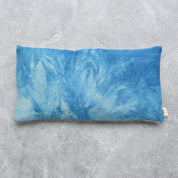 A rectangular eye pillow with a blue and white tie-dye pattern, laid flat on a textured gray concrete surface.