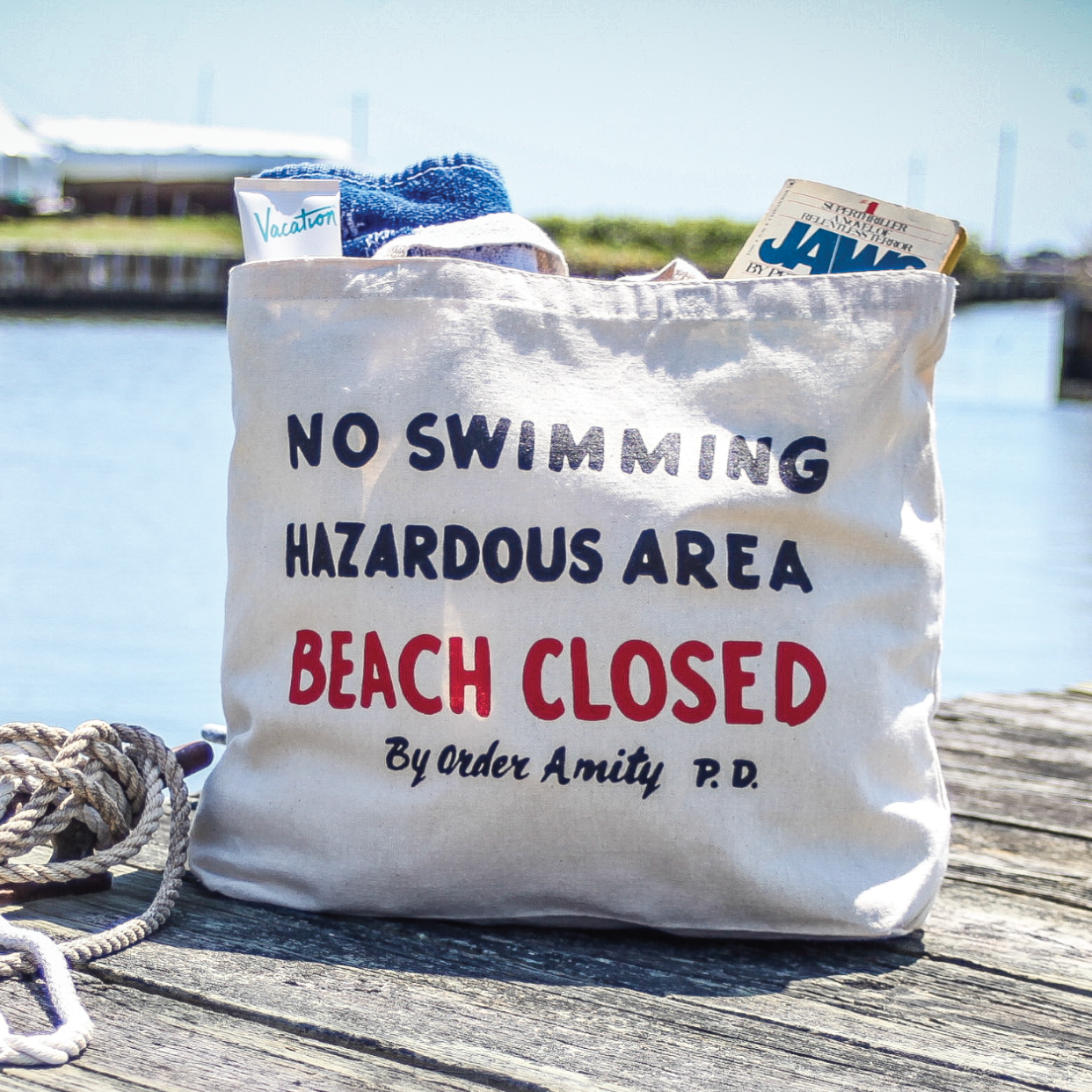 Tote bag with 'No Swimming Hazardous Area Beach Closed' text on a dock by water