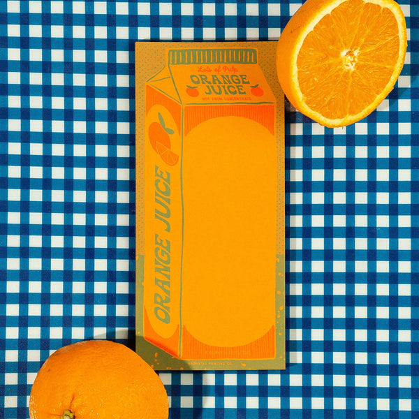 A note pad designed to look like a carton of orange juice with a sliced orange on a blue and white checkered background