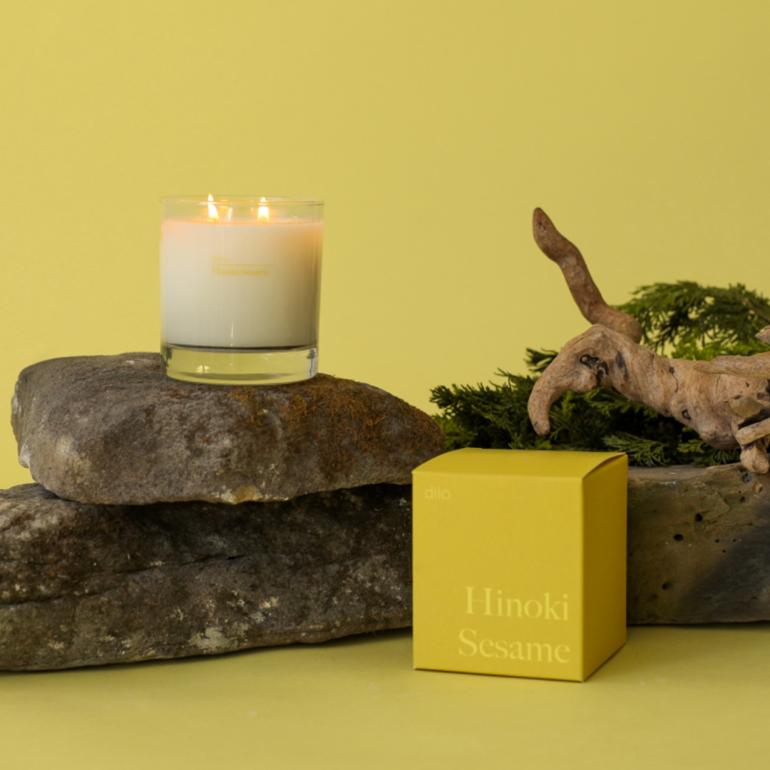 Hinoki Sesame Candle by dilo in a glass container, showcasing a warm flame and aromatic wax.