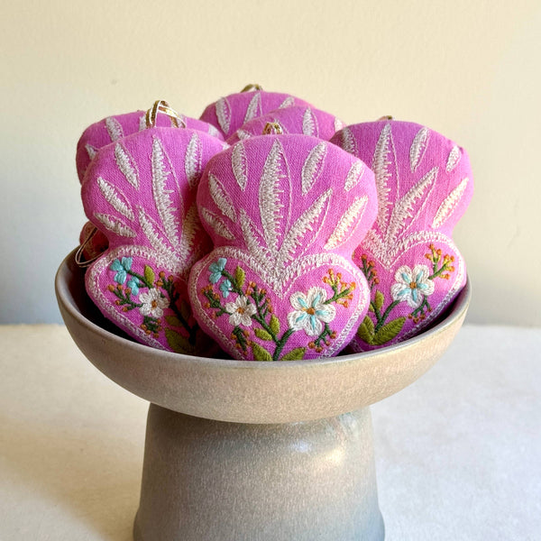Pink heart-shaped fabric items with floral patterns in a gray bowl on a white surface.