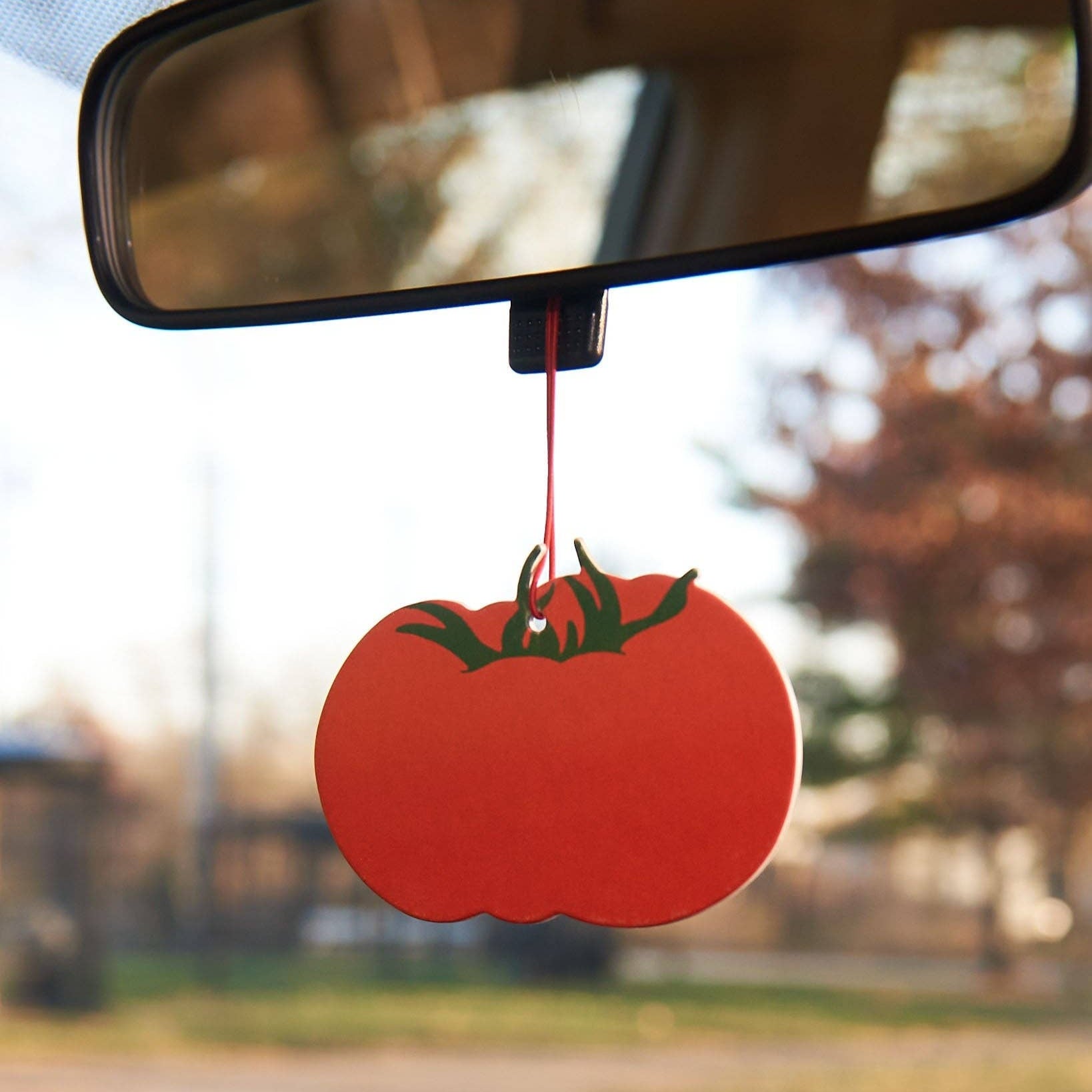 Red tomato-shaped car air freshener hanging from a car's rearview mirror.