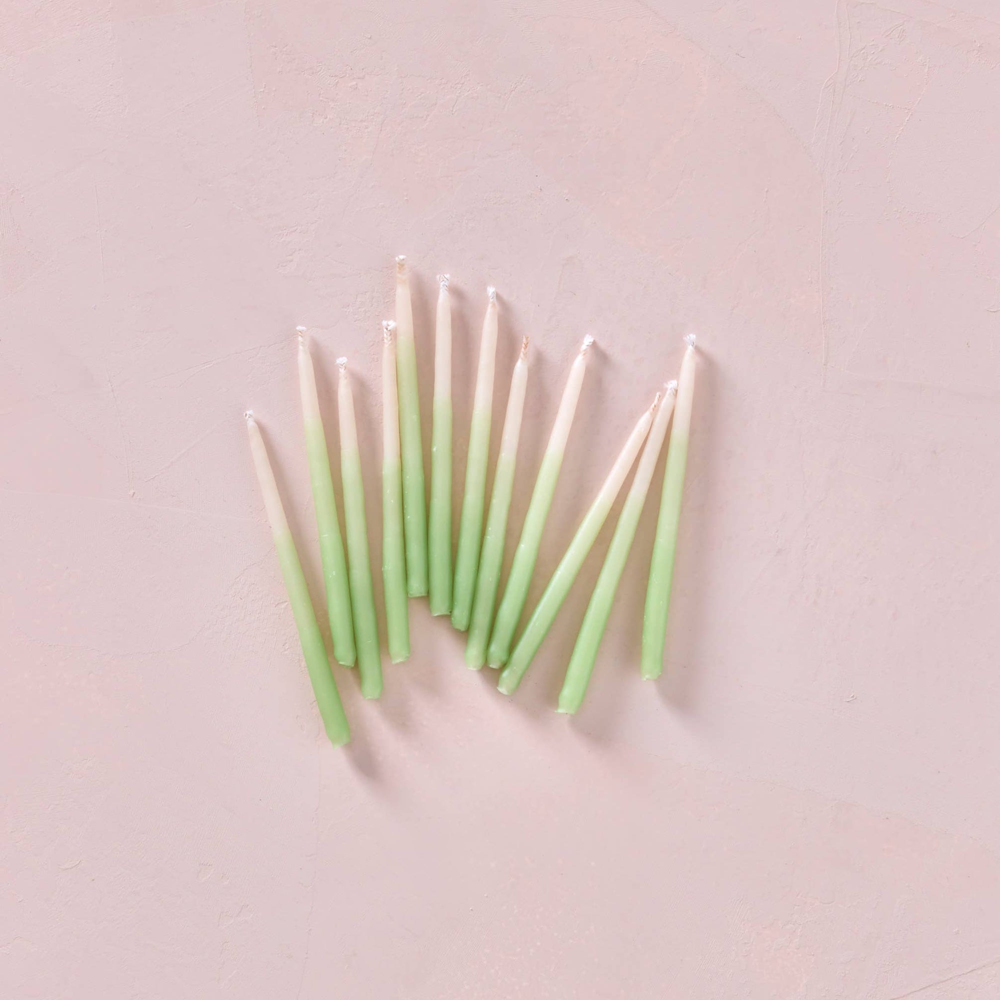 Green candles arranged in a fan-like pattern on a light pink background