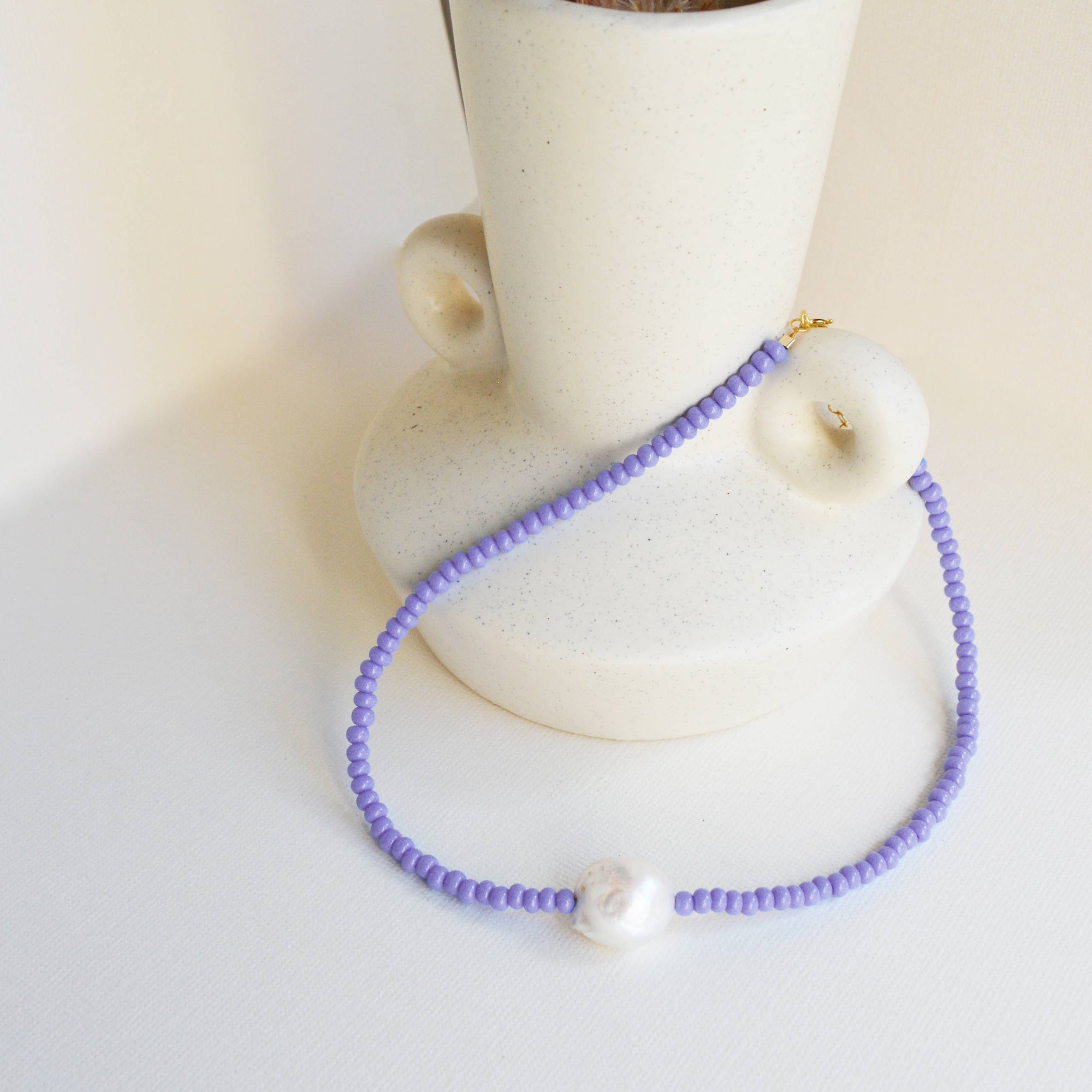 Purple beaded necklace with a white pendant on a white surface