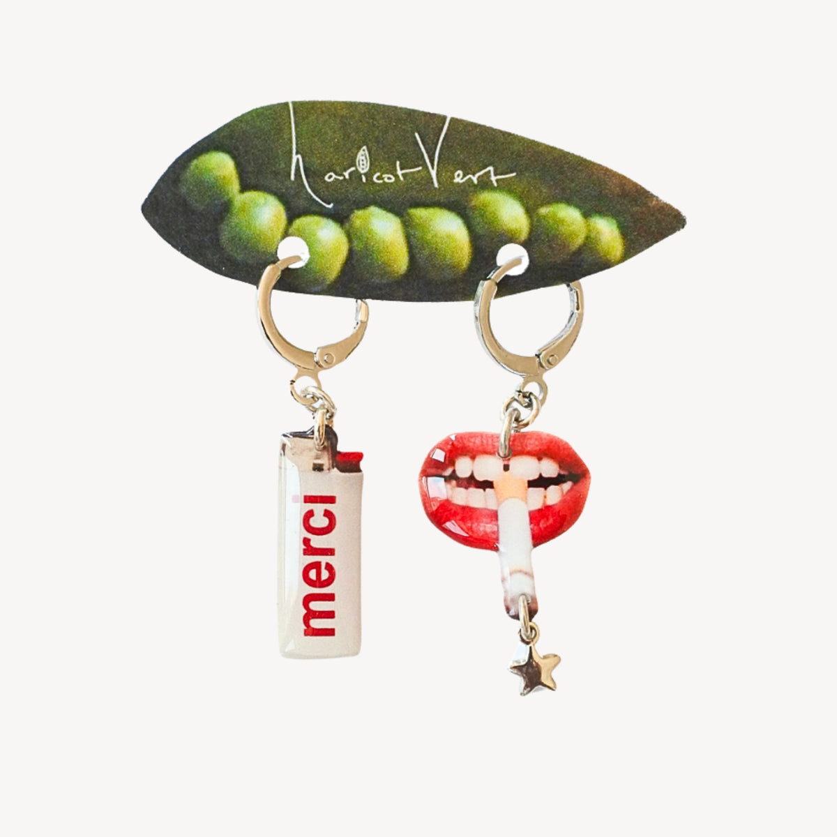 A pair of novelty hoop earrings displayed on a branded leaf-shaped card. One earring hangs from a gold hoop and has a white lighter charm with the red text 'merci'.