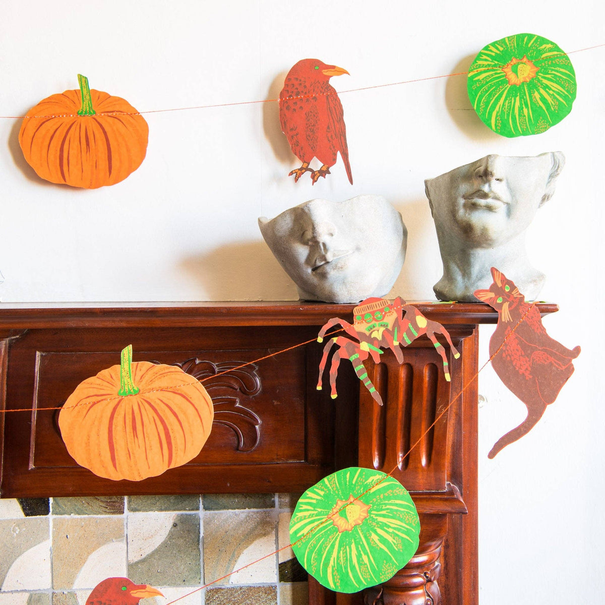 Pumpkin and bird string art Halloween decoration displayed on a dark wooden mantel with ceramic busts against a white wall.
