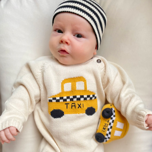 Baby wearing a knitted onesie with a taxi design and a striped hat.
