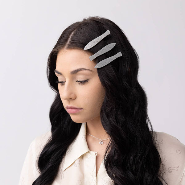 Woman with long dark hair wearing a three sardine barrettes against a light background