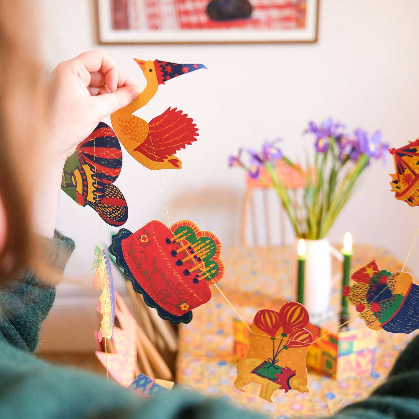 Person holding a colorful swan-shaped object with a decorated table and flowers in the background.