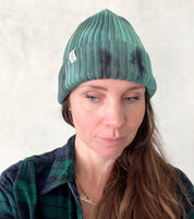 A person wearing a green beanie hat against a light gray background.