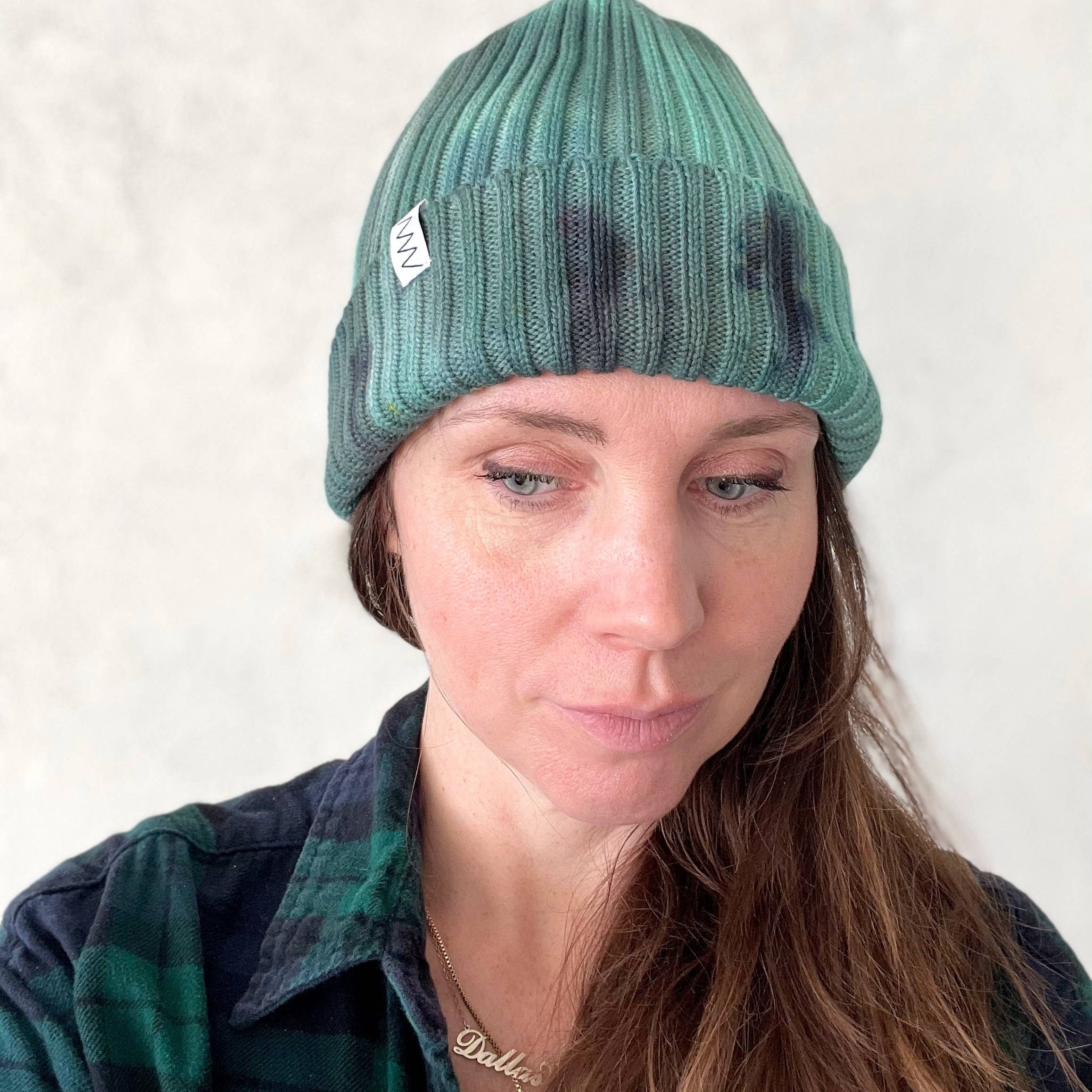 A person wearing a green beanie hat against a light gray background.