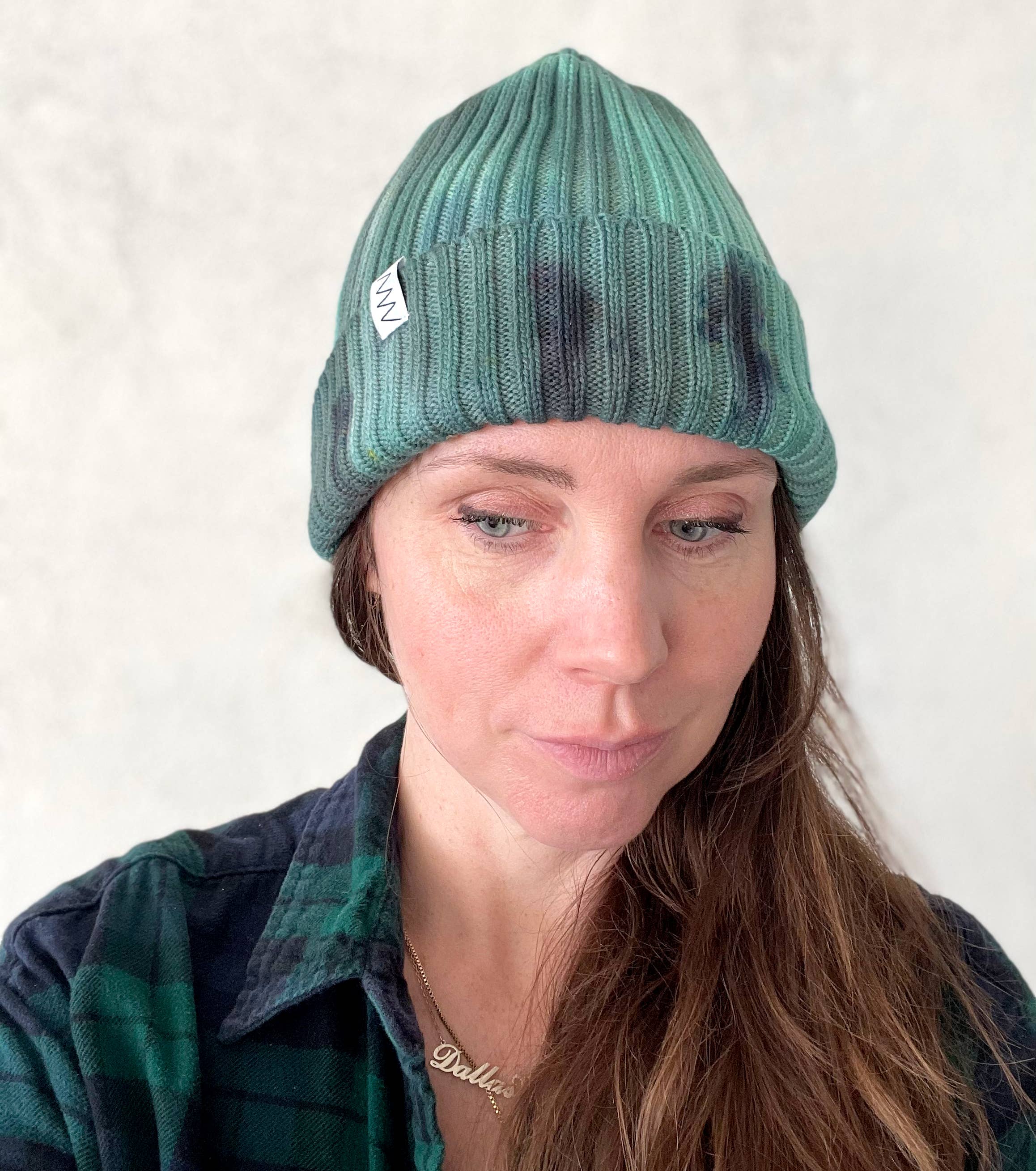 A person wearing a green beanie hat against a light gray background.
