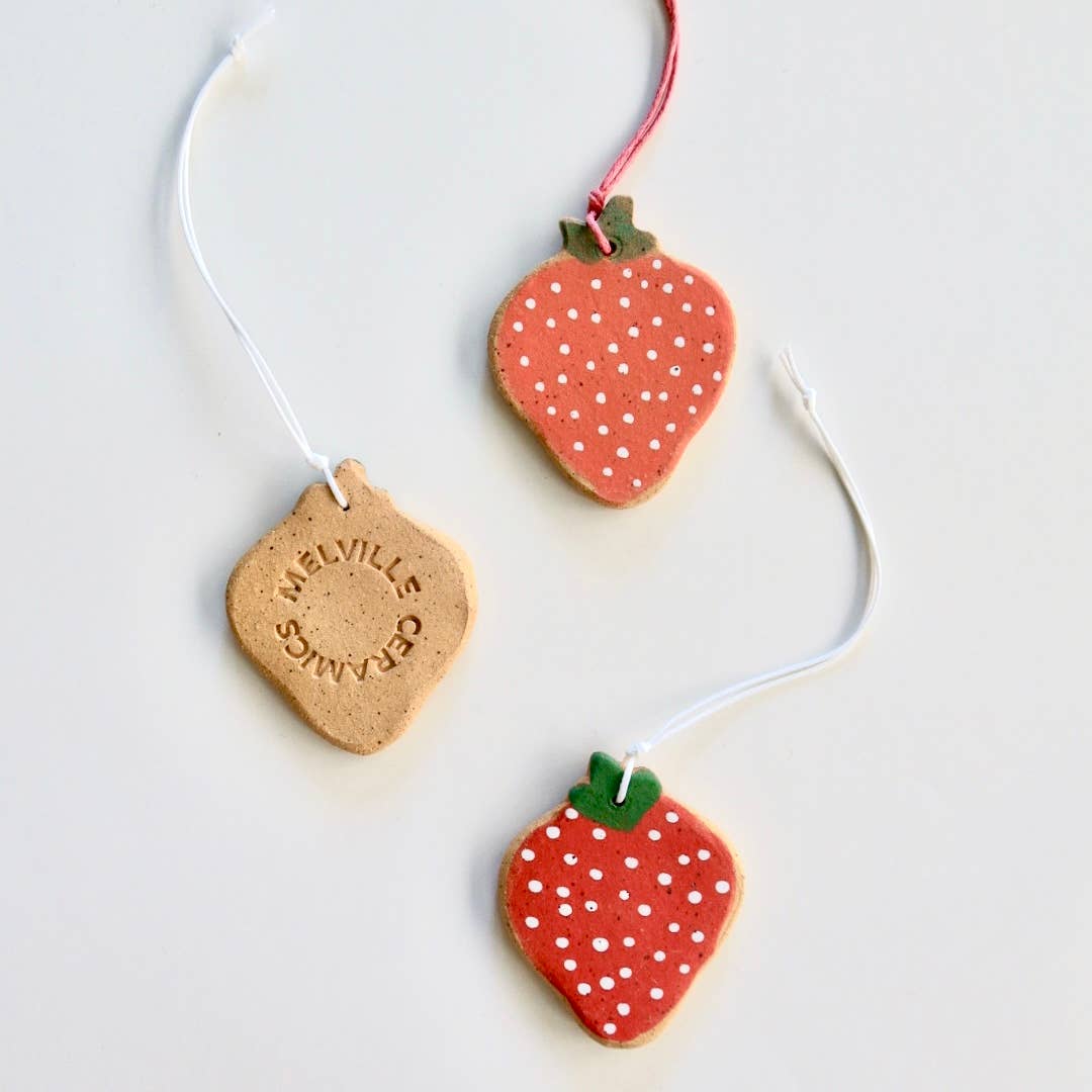 Three ceramic strawberry ornaments with hand painted details, strung with nylon chords.