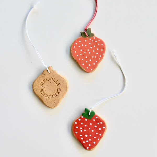 Three ceramic strawberry ornaments with hand painted details, strung with nylon chords.