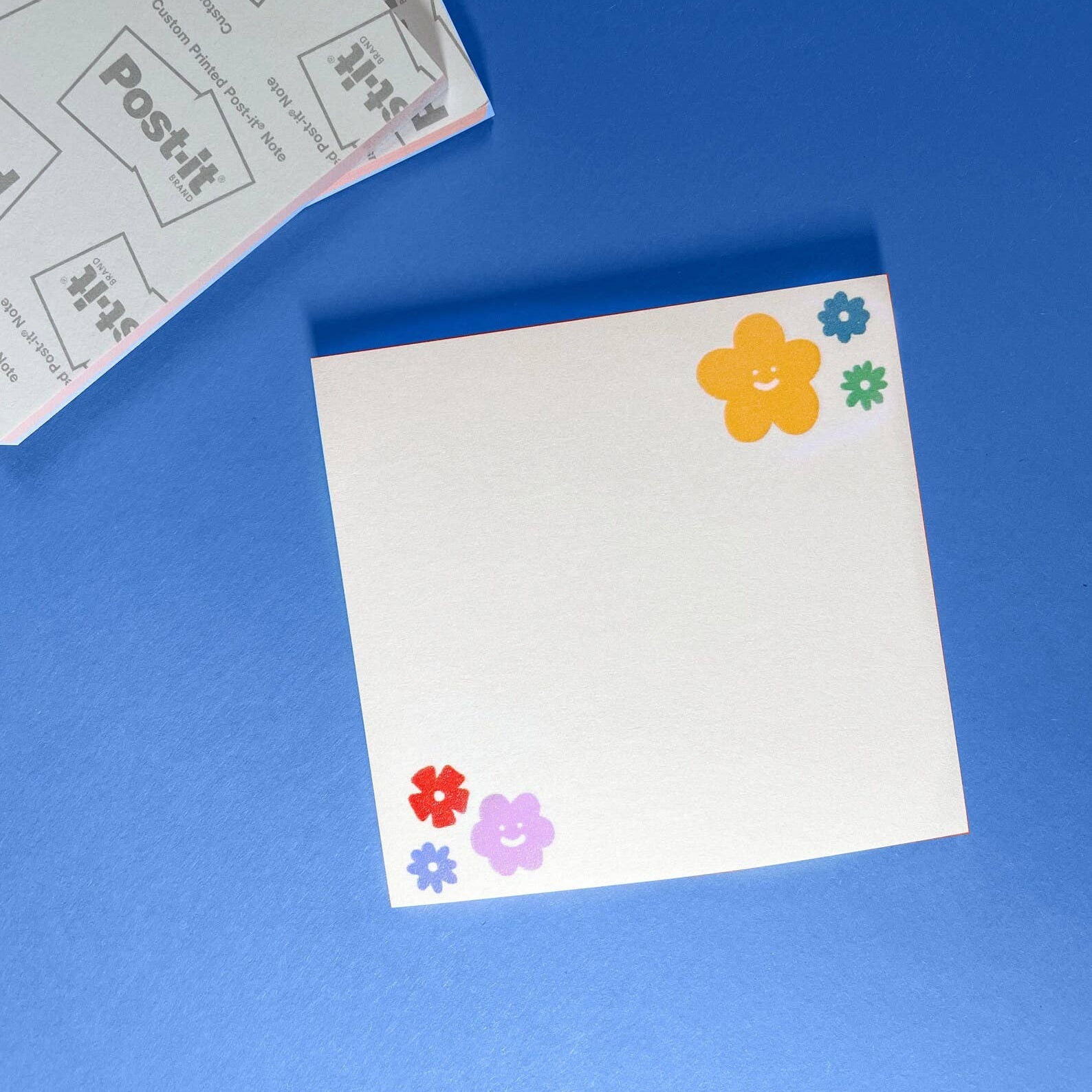White post-it note with colorful flower stickers on a blue background