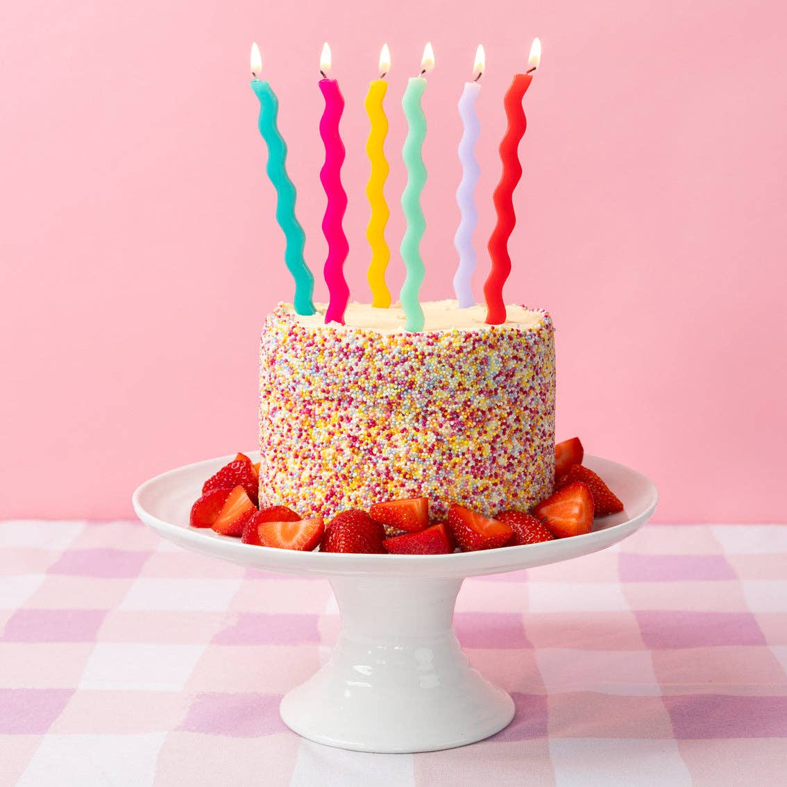 Birthday cake with colorful candles on a pink checkered tablecloth