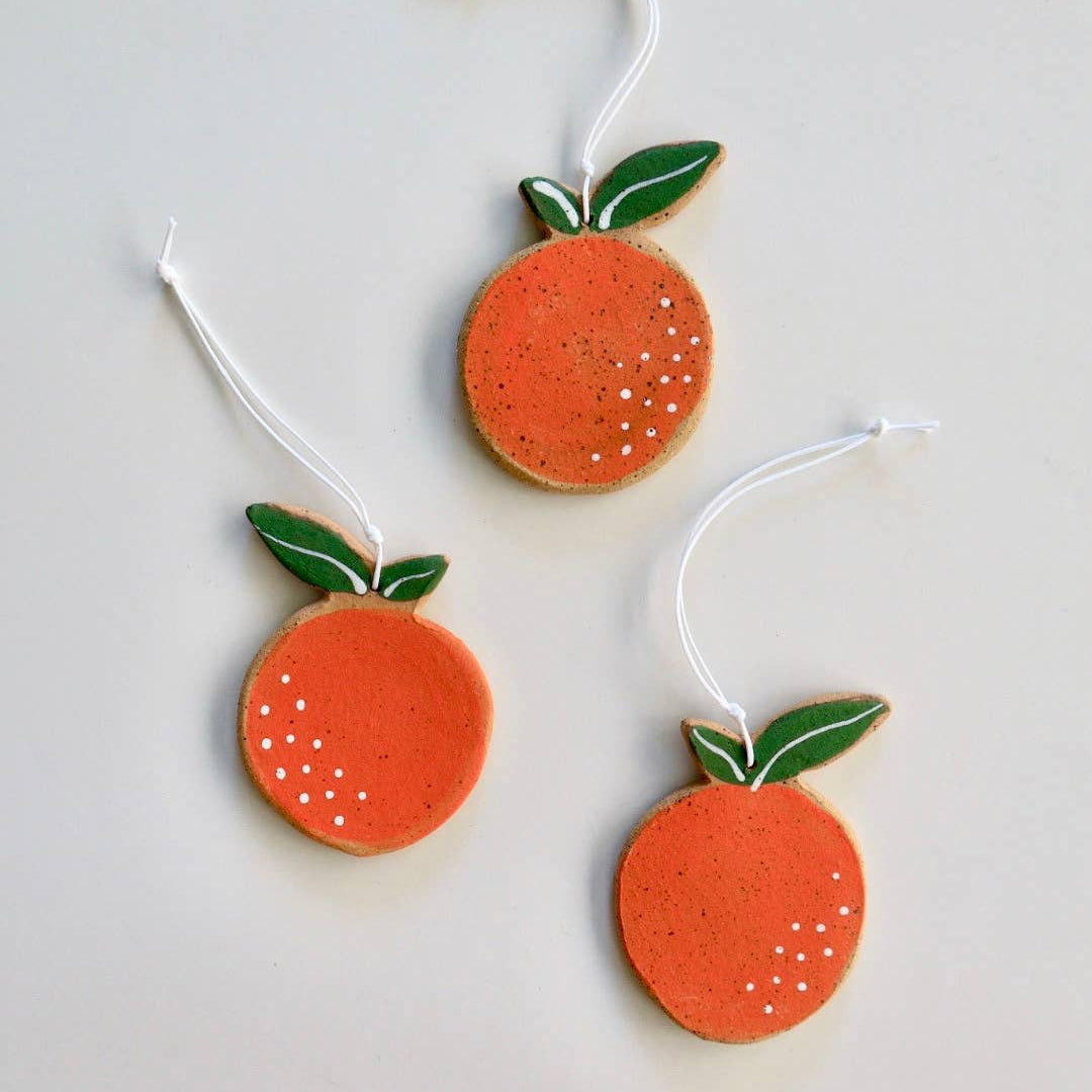 Three handmade ceramic orange ornaments with green stems, each with white hanging tags.
