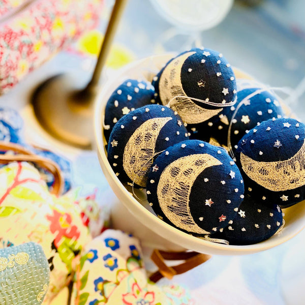 Decorative ornaments with moon and star designs in a bowl on a colorful fabric background