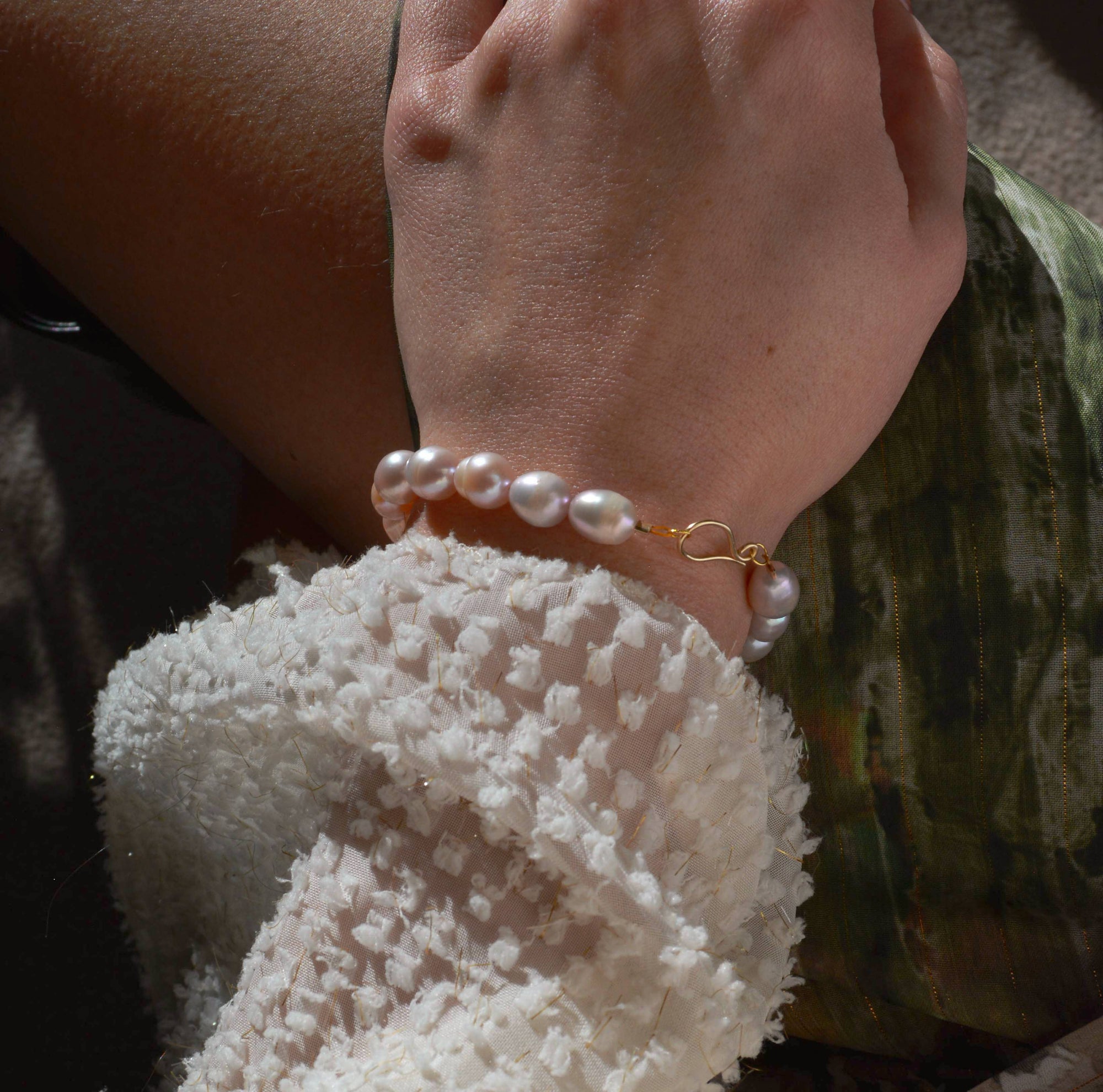 Close-up of a hand wearing a pearl bracelet with a blurred background